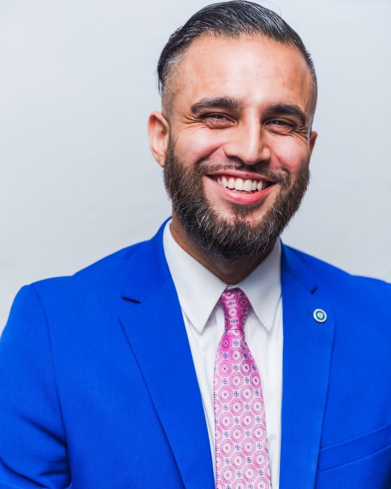 Omar Bhatti, in a blue suit, mid-laugh.
